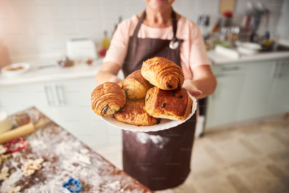 Selective focus photo of a plate with croissants being held by a lady in an apron