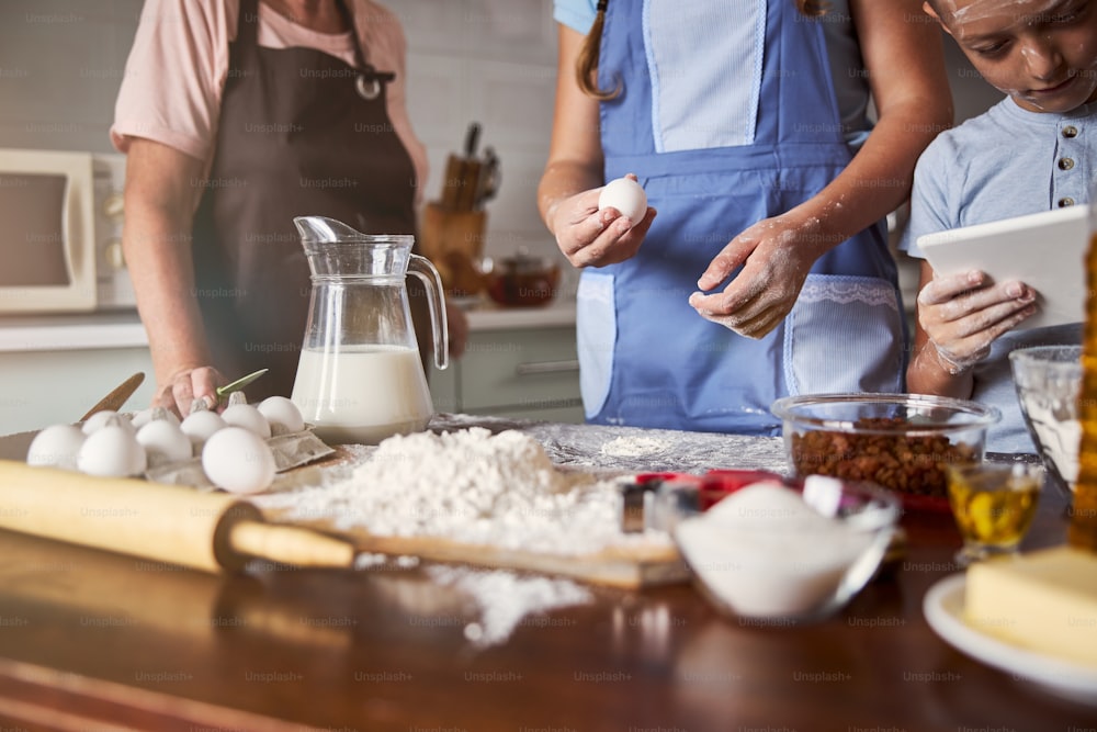 Cropped photo of focused children making progress in the kitchen while preparing dough under their grandma guidance