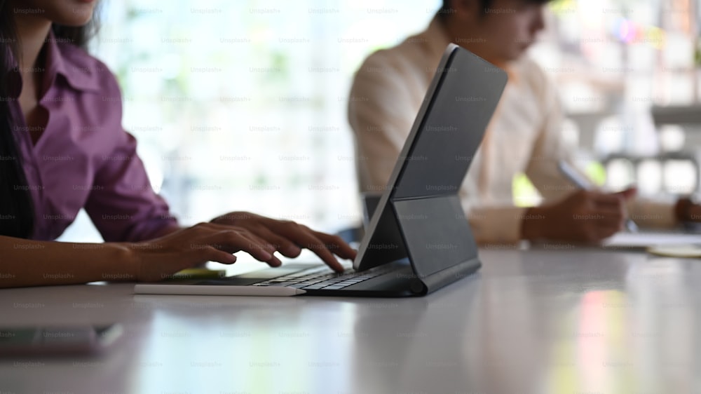 現代のオフィスでコンピュータータブレットを使用して新しいプロジェクトに共同で取り組んでいる2人のビジネス同僚のトリミングショット。