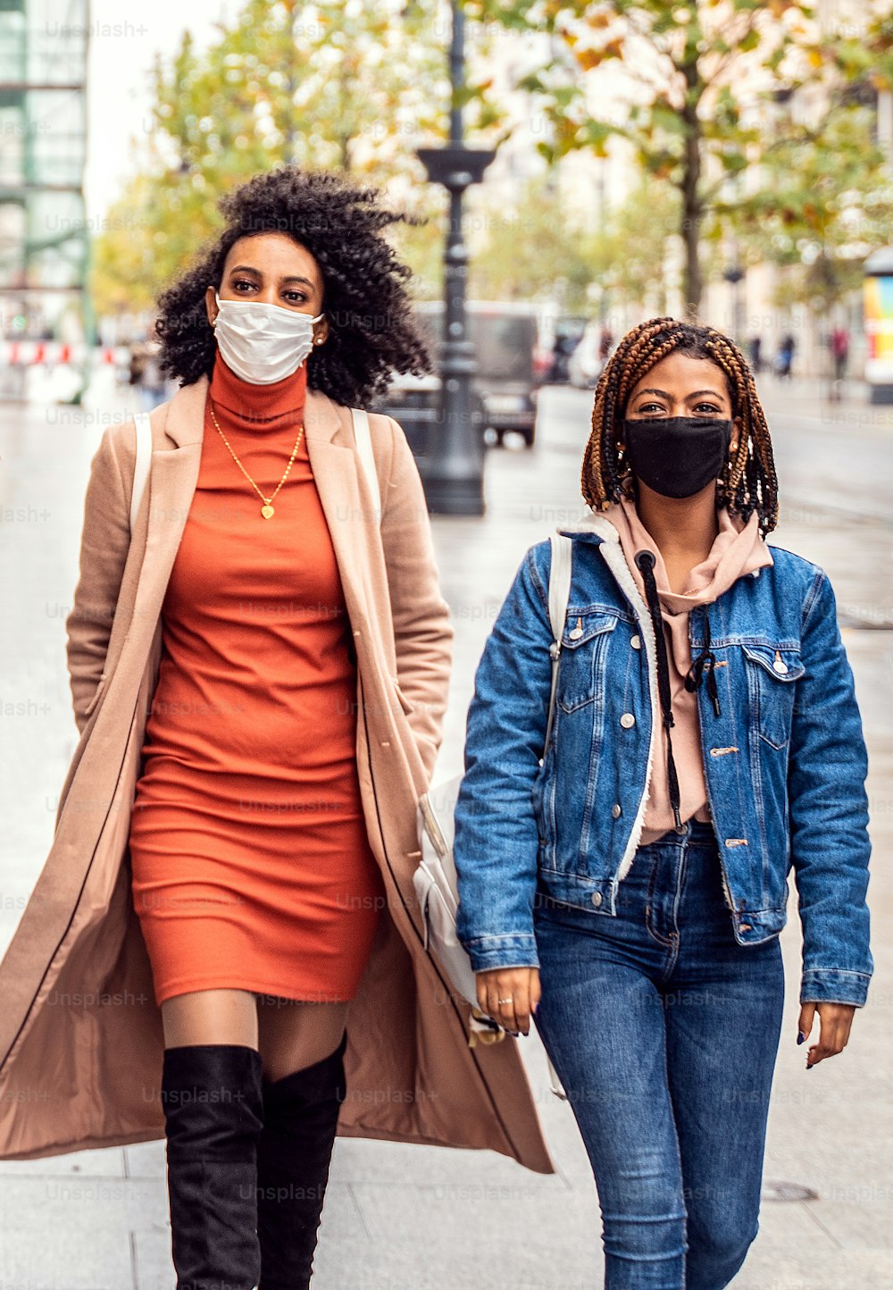 보호용 안면 마스크를 쓰고 도시 거리를 걷고 있는 두 명의 여성 아프리카 친구. 팬데믹 시간. 젊은 사람들의 라이프 스타일 개념입니다.