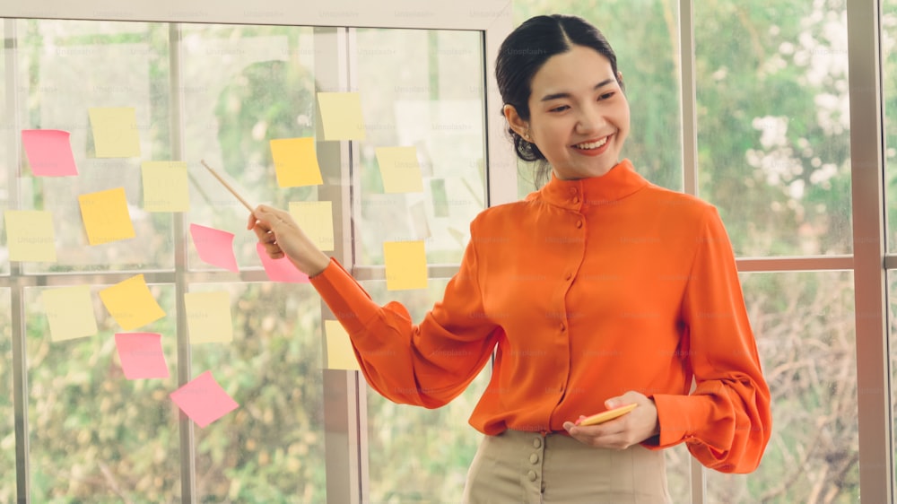 Business people work on project planning board in office and having conversation with coworker friend to analyze project development . They use sticky notes posted on glass wall to make it organized .