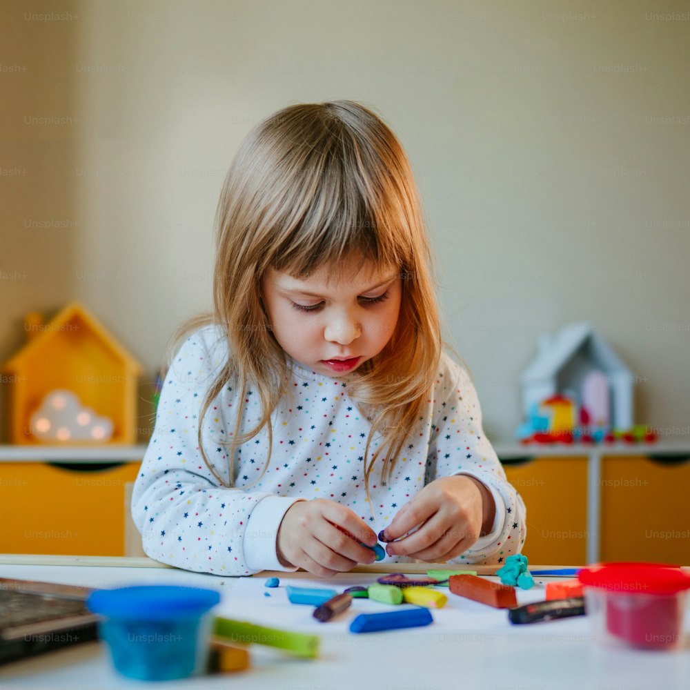 カラフルな粘土を成形する小さな女の子は、屋内のラップトップでオンライン学習レッスンを見ています。遠隔ホーム学習のコンセプト。