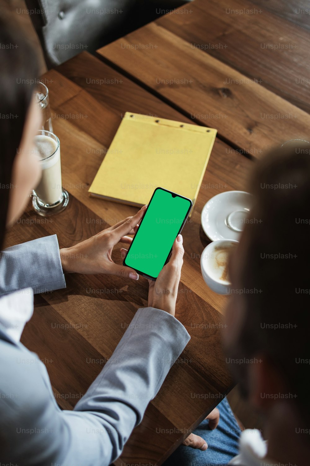 会議や昼食中に、モダンなカフェレストランのビンテージの木製テーブルの上に空白の緑色の画面が付いたスマート携帯電話を持つビジネスマンのモックアップ画像。