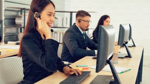 Personas de negocios que usan auriculares que trabajan en la oficina para apoyar a clientes o colegas remotos. El centro de llamadas, el telemarketing y el agente de atención al cliente brindan servicio en llamadas telefónicas de videoconferencia.