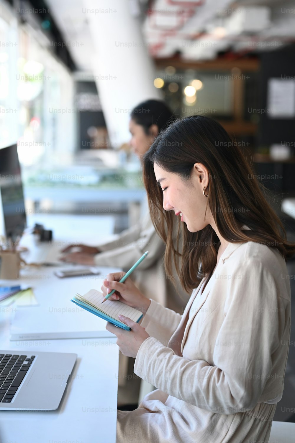 Una giovane donna sorridente che scrive idee sul suo taccuino mentre è seduta in ufficio.