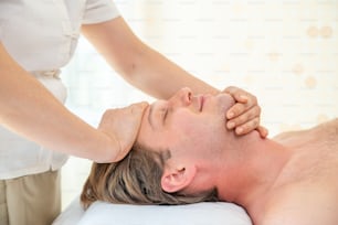 Kaukasischer Mann ruht sich auf dem Massagebett aus und erhält eine Gesichtsbehandlung mit ätherischem Öl von einem professionellen Therapeuten im Schönheitssalon