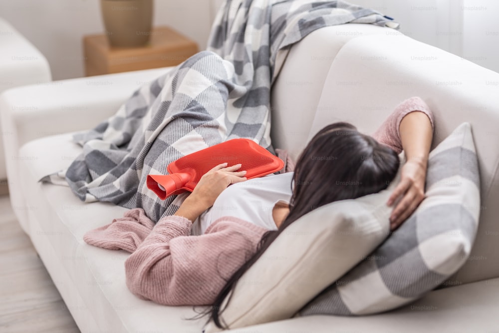 Dor de estômago aliviada por termóforo enquanto a mulher se deita em um sofá sob o cobertor.