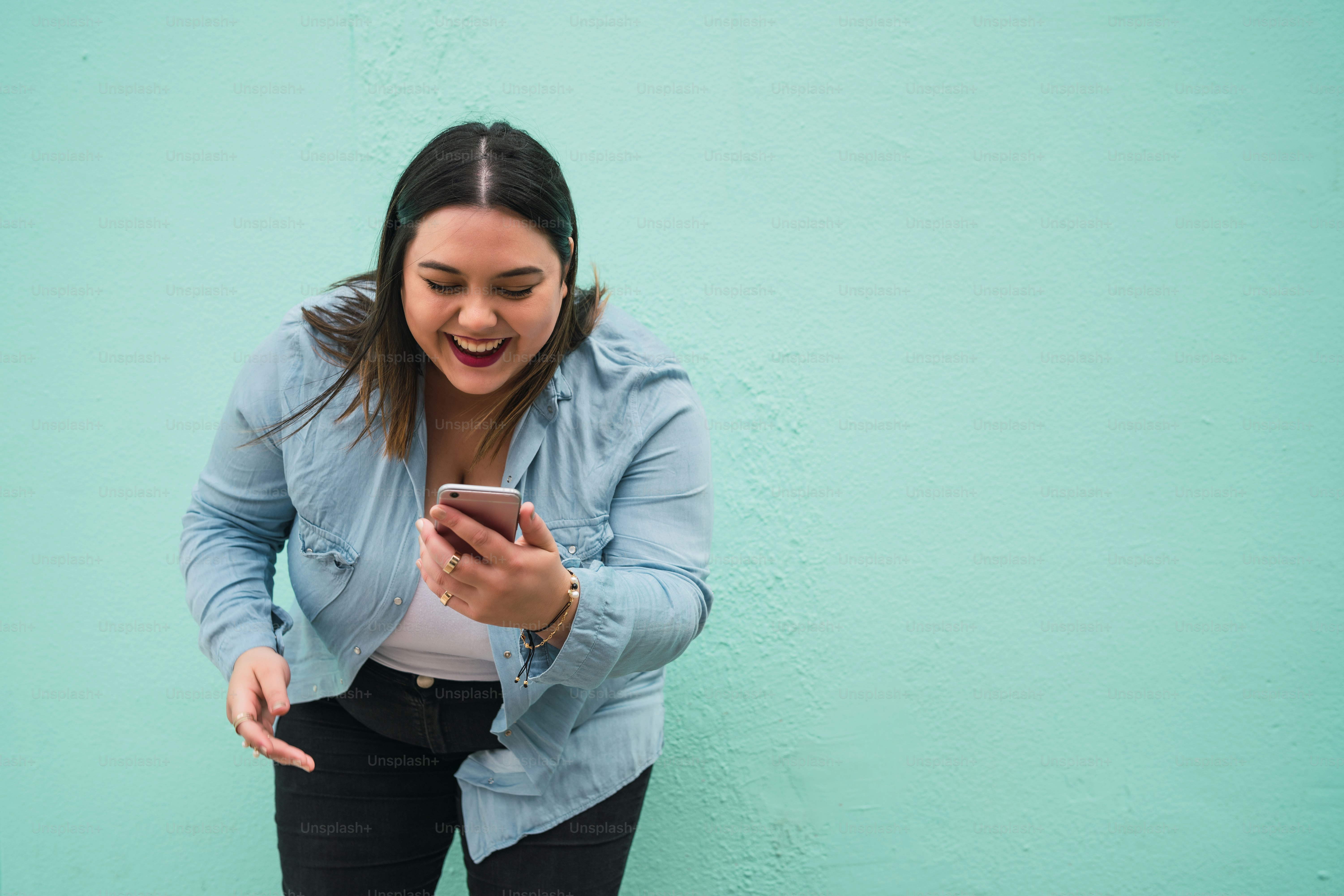 Ritratto di giovane donna plus size che sorride mentre digita un messaggio di testo sul suo telefono cellulare all'aperto. Concetto di tecnologia.
