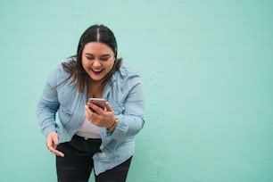 屋外で携帯電話にテキストメッセージを入力しながら微笑む若��いプラスサイズの女性の肖像画。テクノロジーコンセプト。