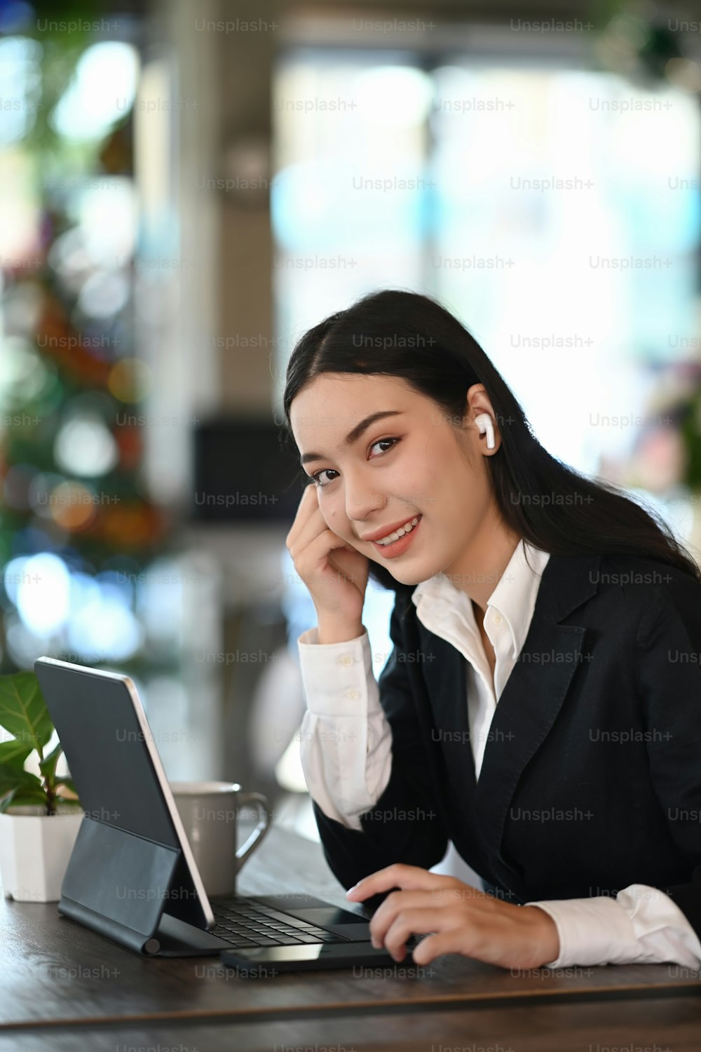 Retrato de uma jovem empresária com fones de ouvido sem fio está sorrindo para a câmera enquanto trabalha em seu local de trabalho.