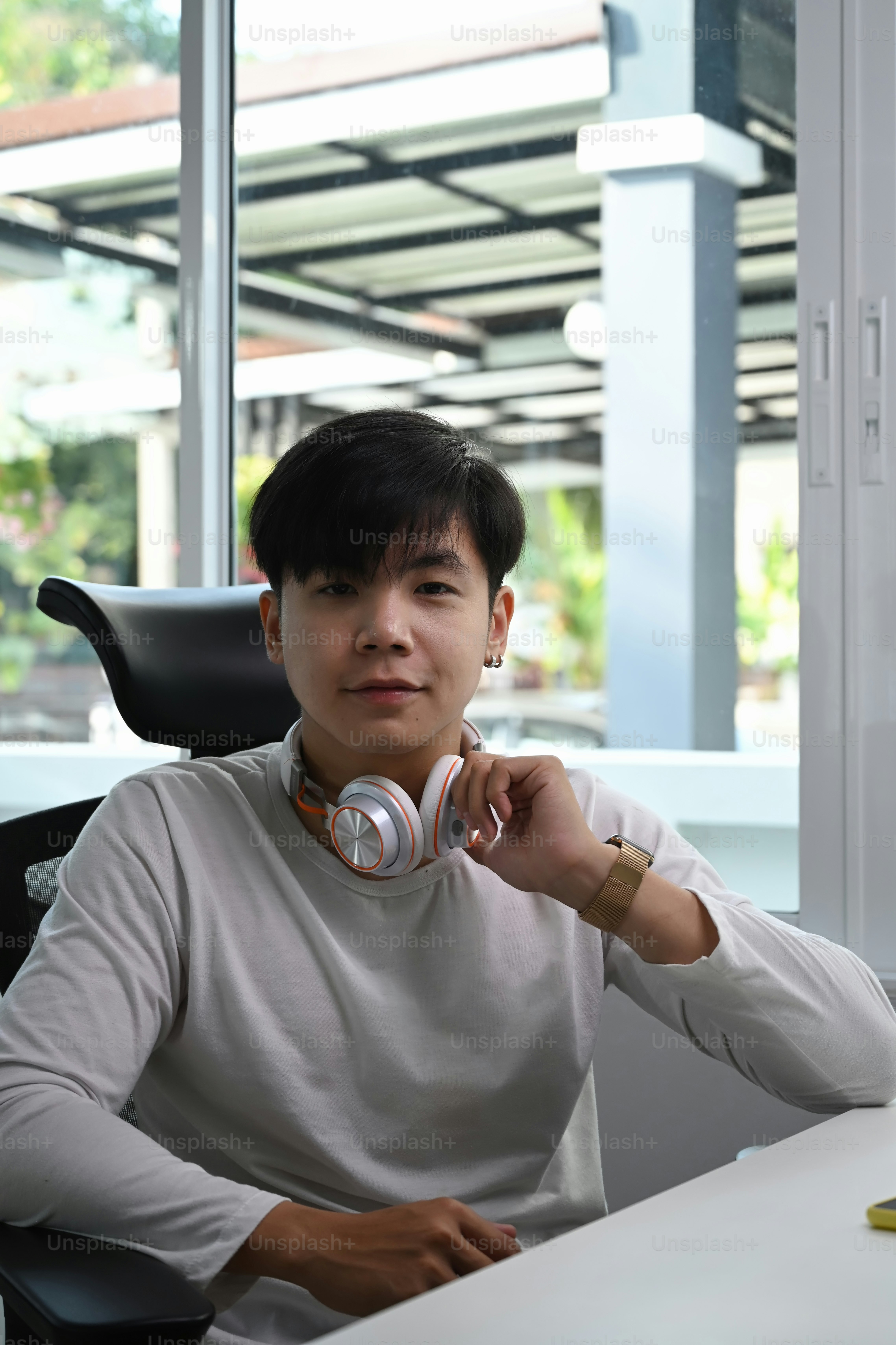 Portrait of a cheerful young man with headphone sitting in office and smiling to camera.