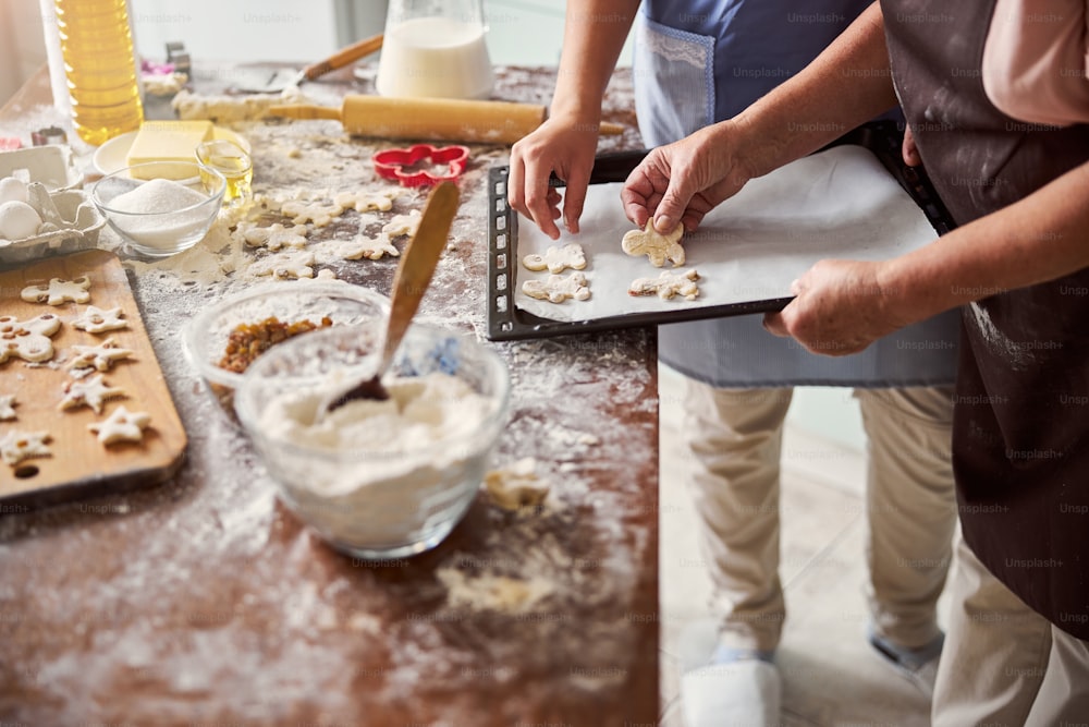 Cropped photo of two people involved into cookie baking process in cozy kitchen