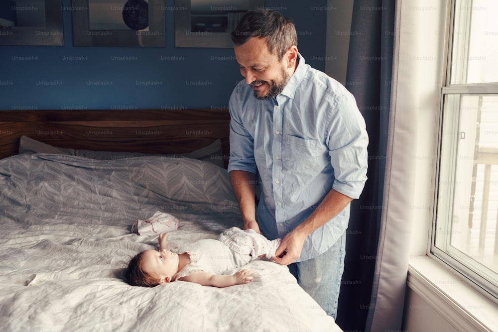 Middle age Caucasian father changing diaper clothes for newborn baby daughter son. Man parent taking care of child at home. Authentic lifestyle candid moment. Single dad family day life.