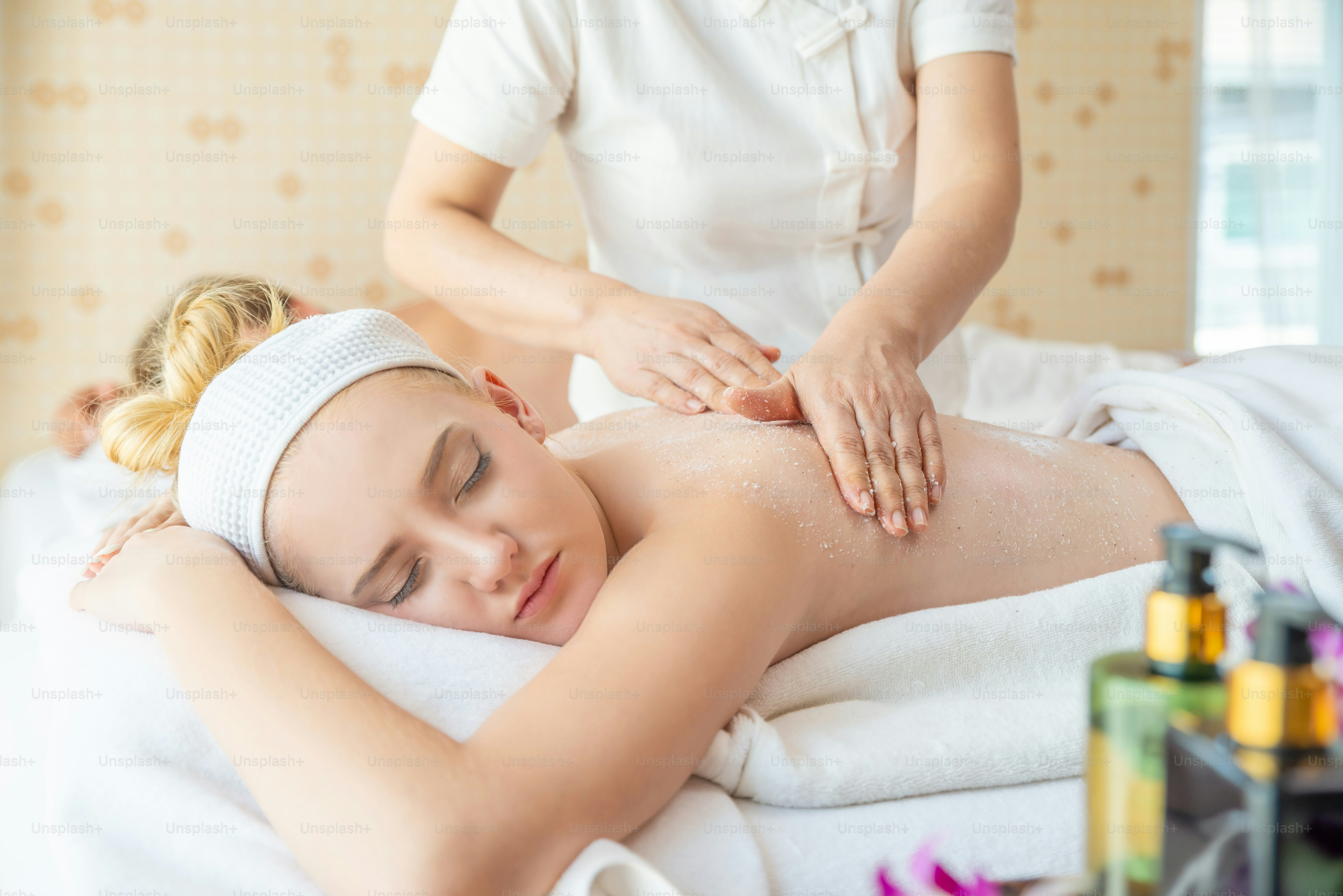 Wanita Kaukasia berbaring di tempat tidur spa mendapatkan kembali pijat lulur dengan garam spa di salon kecantikan