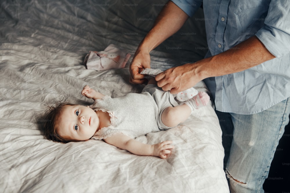 Father changing diaper put on clothes for newborn daughter. Cute baby looking into camera. Man parent taking care of child at home. Authentic lifestyle candid moment. Single dad family day life.