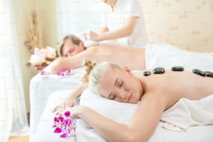 Mujer caucásica que descansa en una cama de masaje y vuelve a recibir un tratamiento de spa con aceite esencial y piedras calientes de un terapeuta profesional