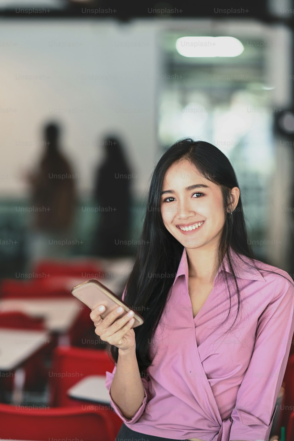 Retrato de una joven empresaria asiática sostiene un teléfono móvil mientras sonríe a la cámara en la oficina.