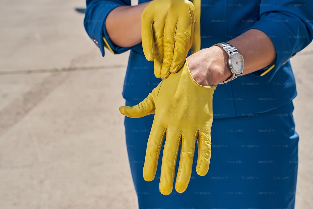 Foto recortada de una azafata joven y delgada en uniforme poniéndose un guante en la mano