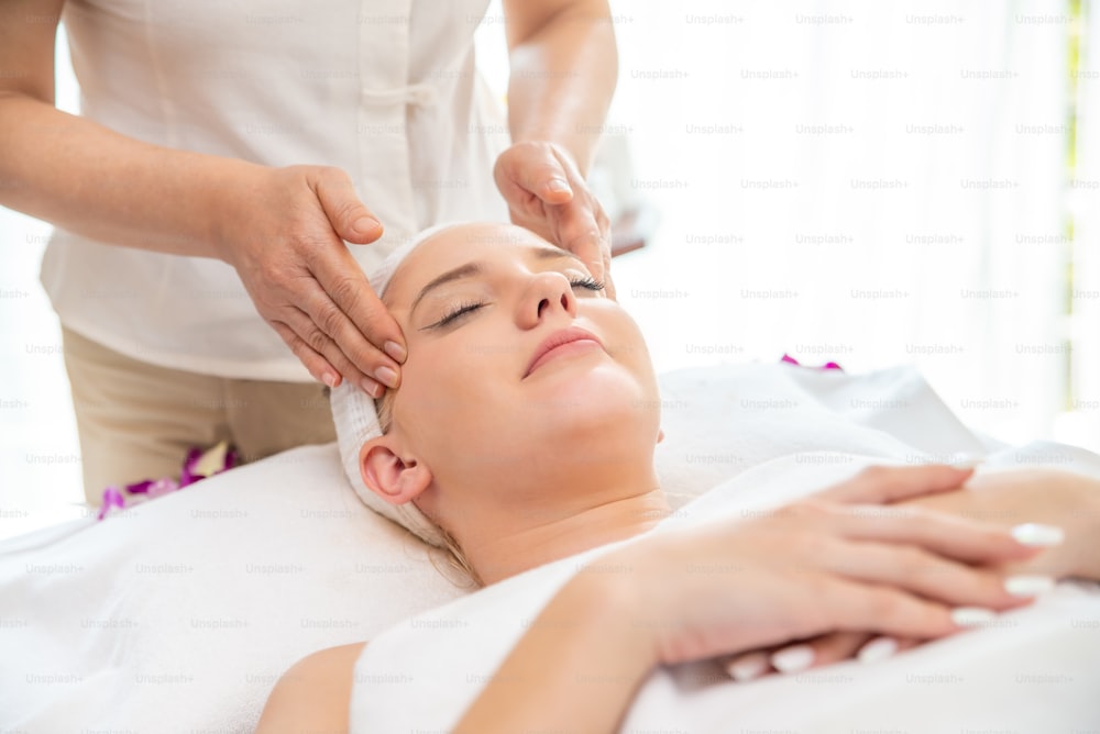 Donna caucasica che riposa sul lettino da massaggio e ottiene un trattamento termale facciale con olio essenziale da un terapeuta professionista nel salone di bellezza