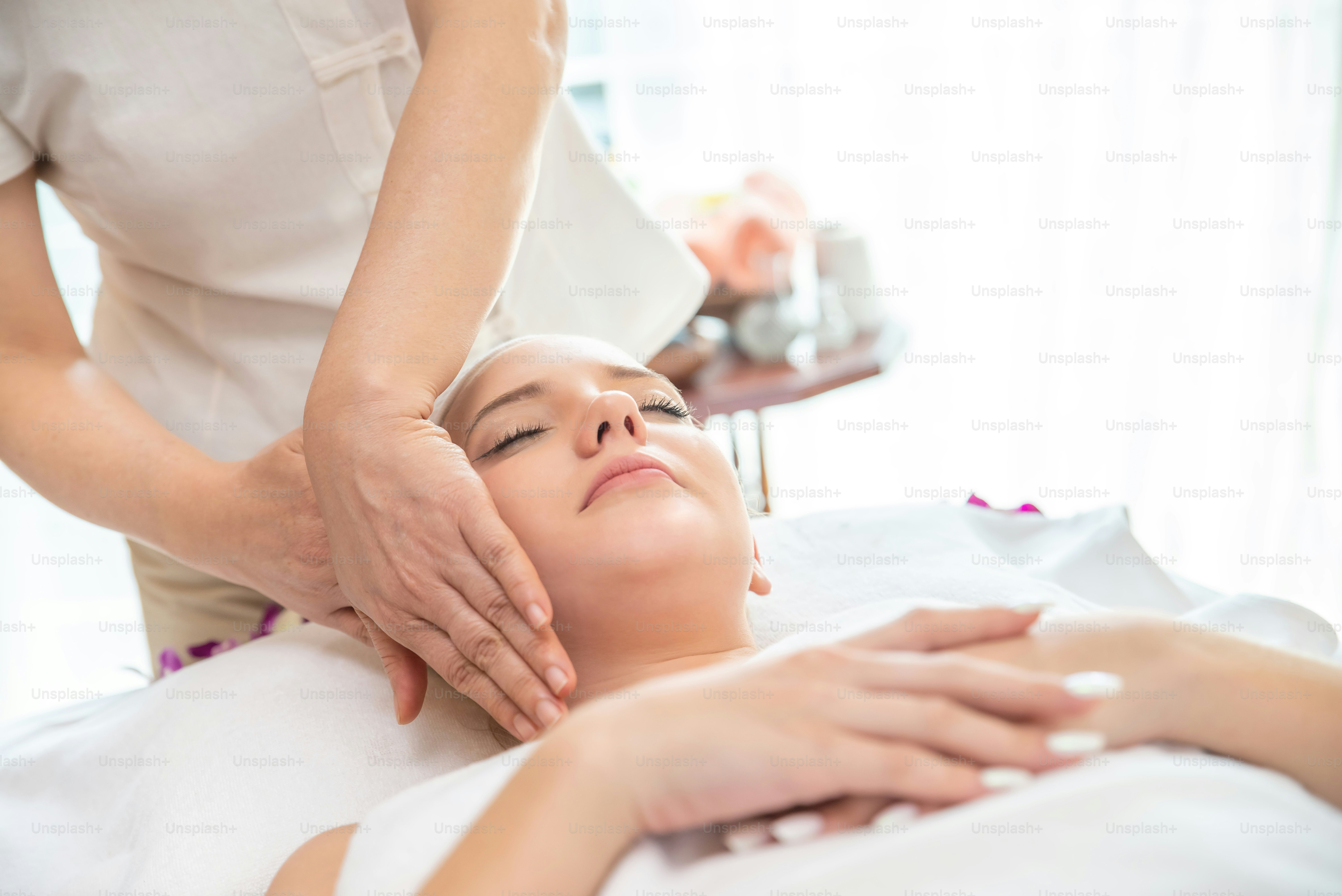 Wanita Kaukasia beristirahat di tempat tidur pijat dan mendapatkan perawatan spa wajah dengan minyak esensial dari terapis profesional di salon kecantikan