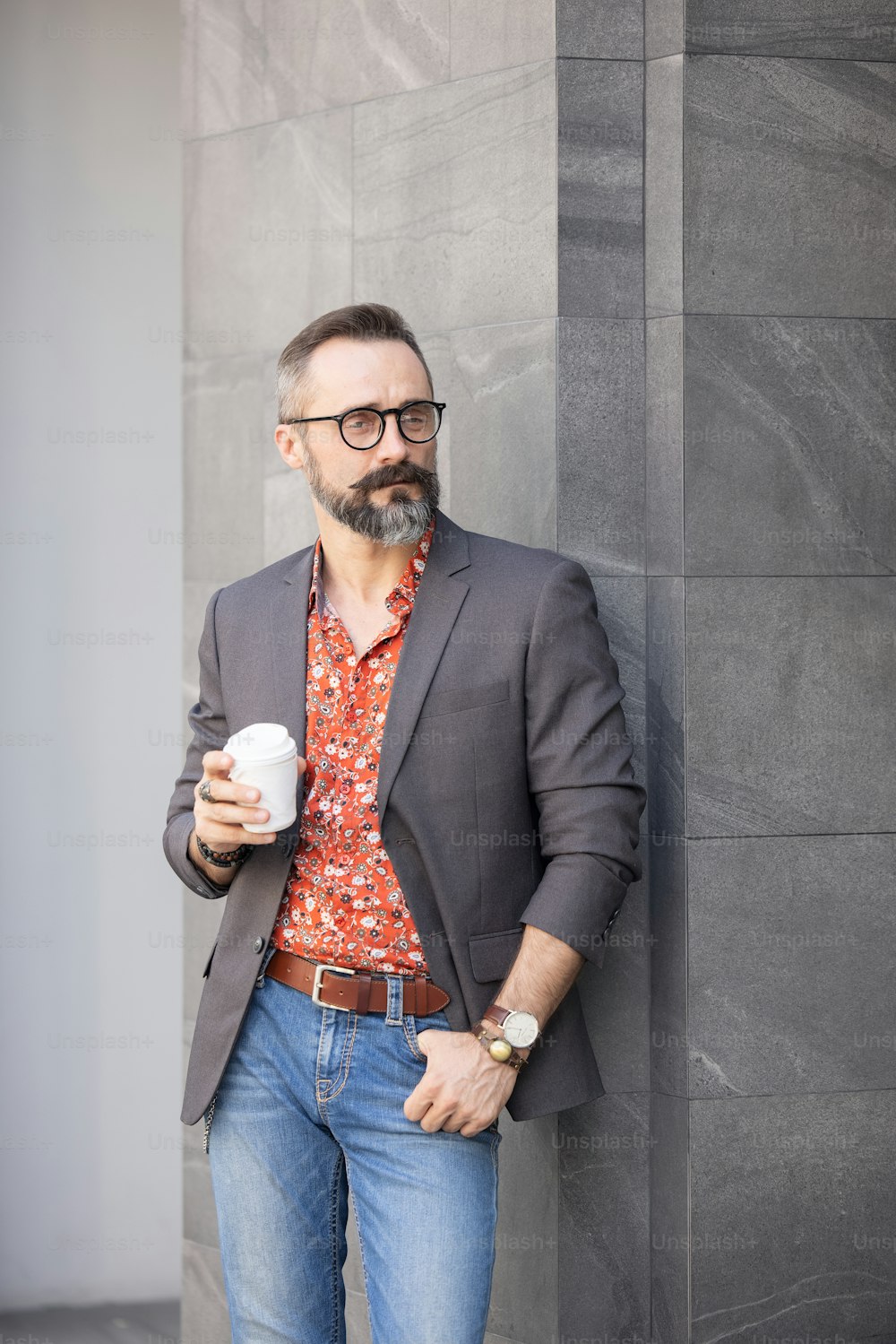 Handsome cheerful man standing near office building holding disposable cup coffee
