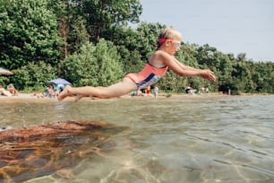Cute funny Caucasian girl diving in lake with underwater goggles. Child swimming in water on Awenda beach. Authentic real lifestyle happy childhood. Summer fun outdoor seasonal activity.