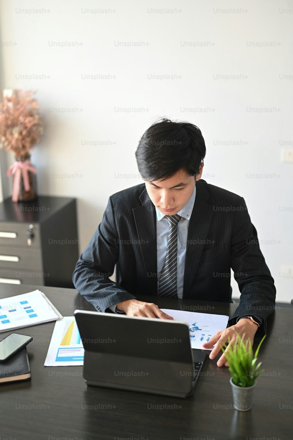 Portrait of businessman in black suit using computer tablet and analyzing data in office.