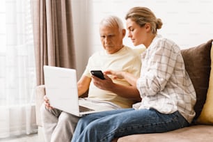 Mulher nova explicando ao homem idoso como usar laptop e smatphone