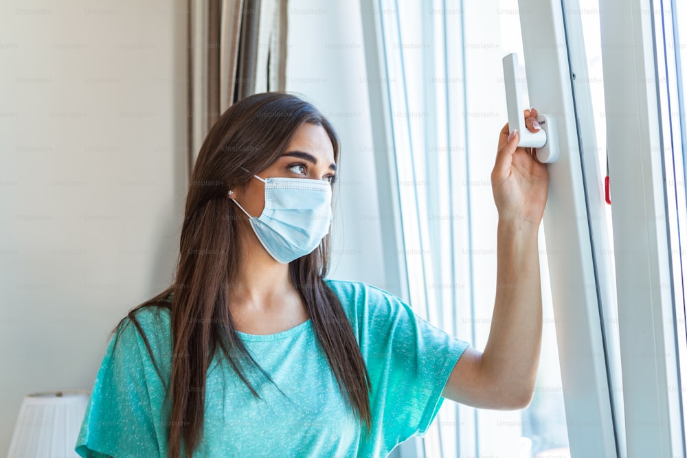 Home quarantine. Caucasian woman sitting at window in a medical mask, looking out, wants to go out. protection against coronavirus infection, pandemics, disease outbreaks and epidemics.