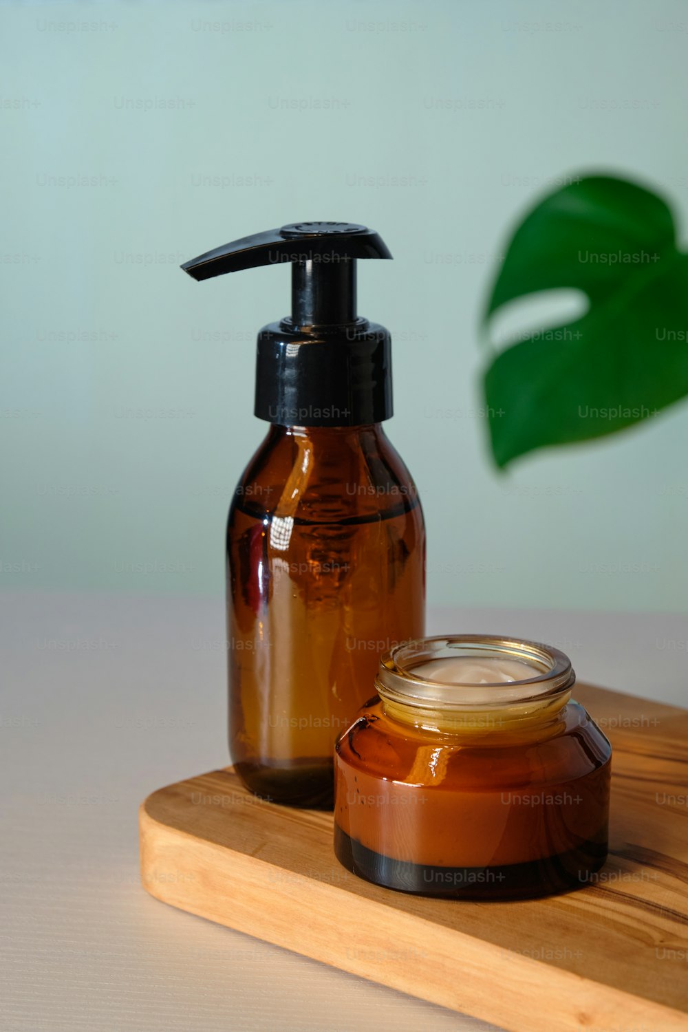 Amber glass cosmetics bottle on wooden board and tropical plant leaf. Natural organic beauty product in pump bottle and jar of moisturizer cream.