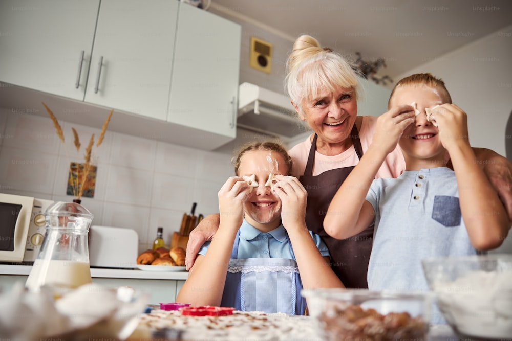 Senhora idosa alegre abraçando seus netos com massa de biscoito em forma de estrela em suas mãos