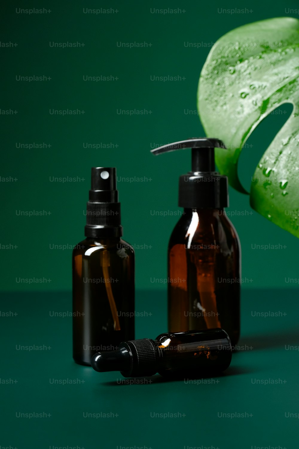 Conjunto de botellas cosméticas de vidrio ámbar y hoja de monstera sobre fondo verde. Envases de productos de belleza ecológicos naturales sin etiquetas.