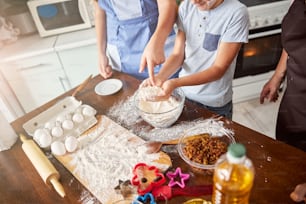 Cropped photo of two children touching food ingredients while making creative mess on the kitchen table