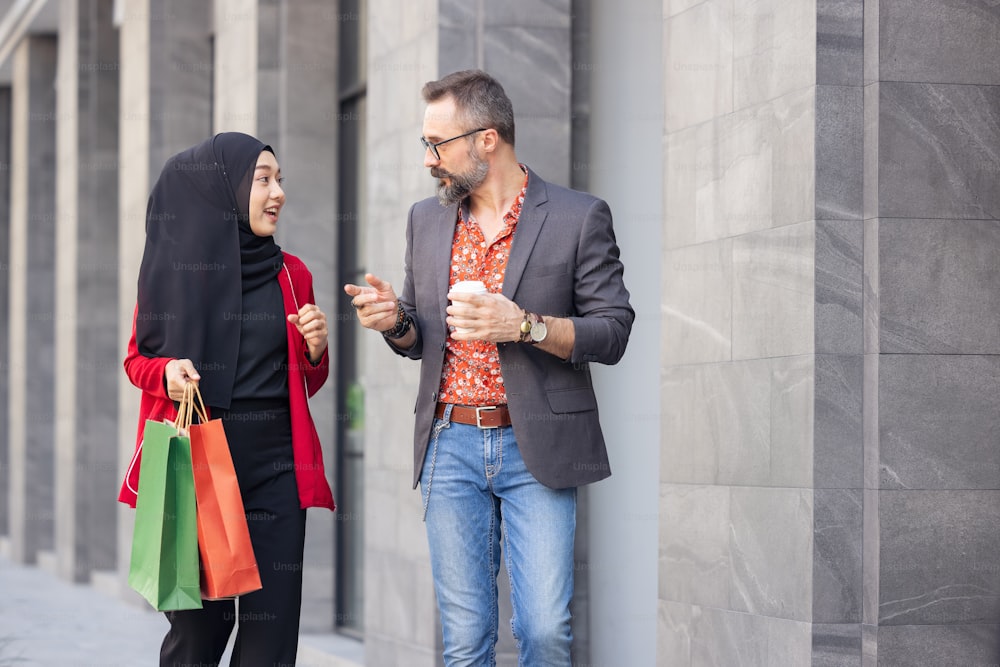 Femme musulmane heureuse et petit ami avec des sacs en papier tenant à la main des achats en ville