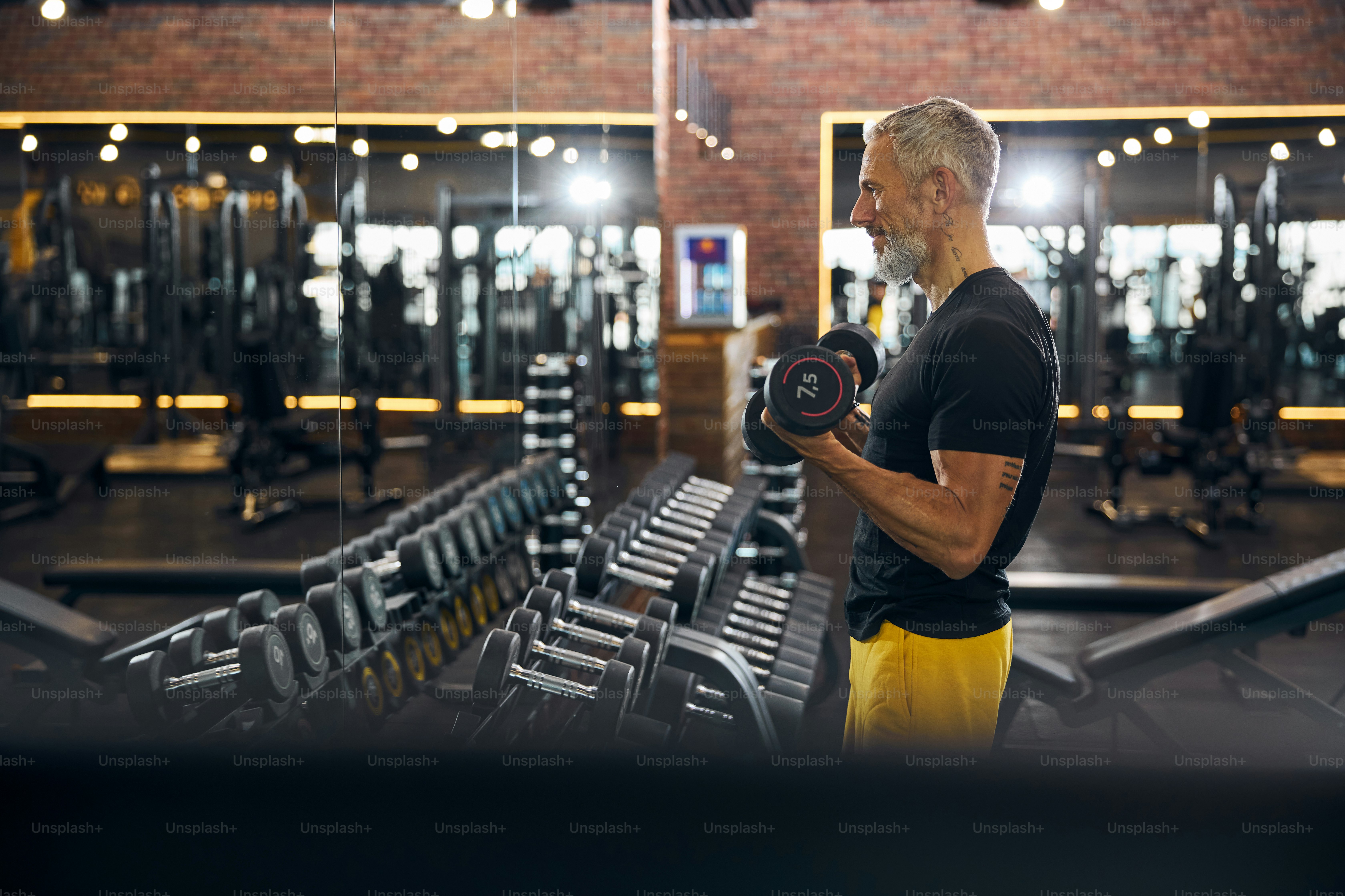 Side view of a smiling sportsman working out with dumbbells in front of the mirror