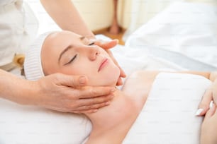 Mujer caucásica que descansa en una cama de masaje y recibe un tratamiento de spa facial con aceite esencial de un terapeuta profesional en el salón de belleza