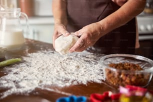 Cropped photo of senior person hands holding a chunk of dough above the kitchen table