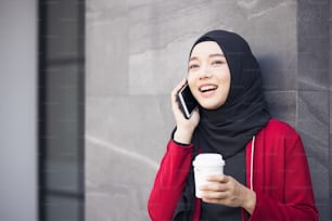 Operazione riuscita. Donne d'affari arabe in hijab che tengono un caffè per strada e tengono in mano un telefono cellulare