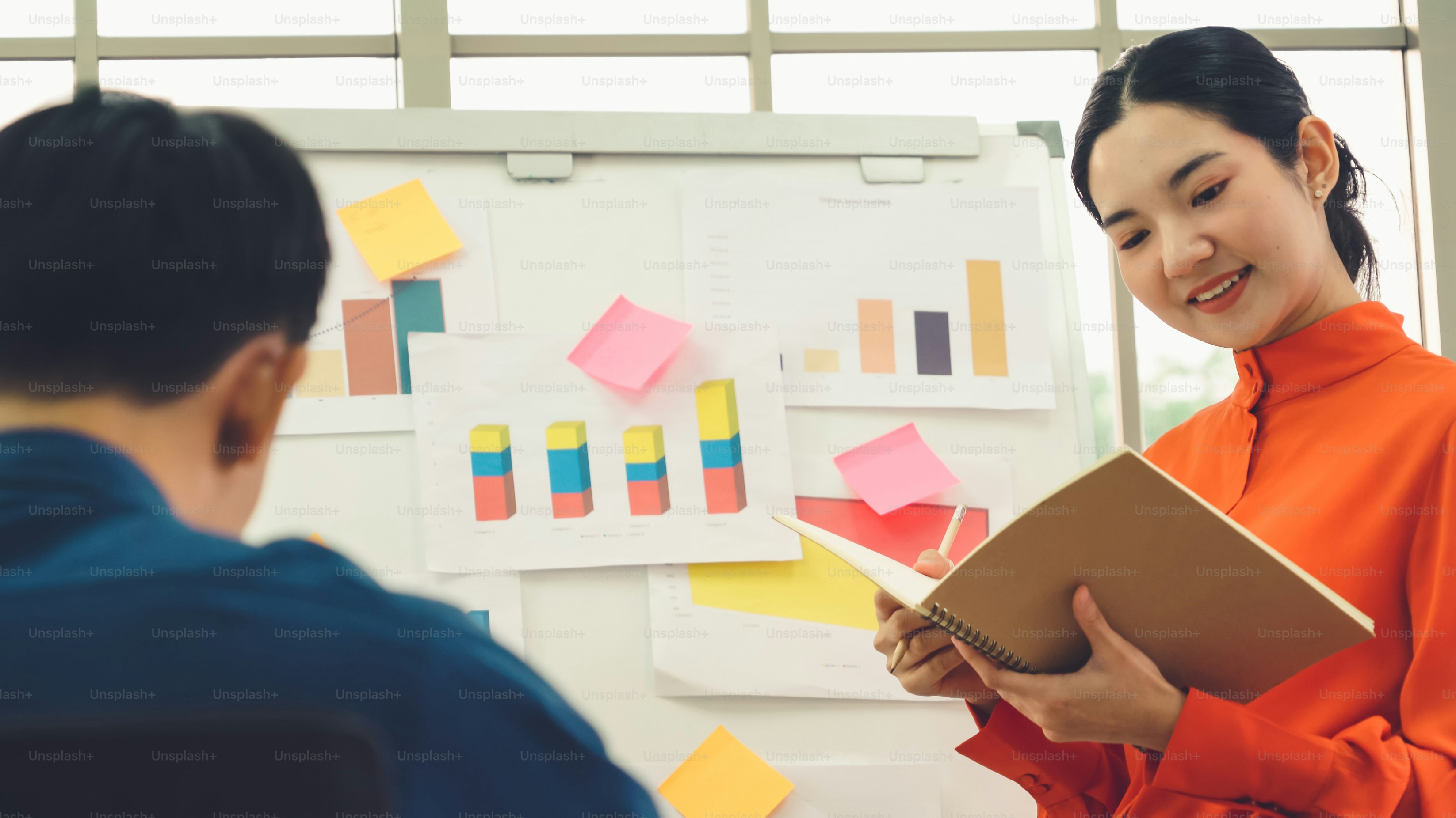 Young woman explains business data on white board in casual office room . The confident Asian businesswoman reports information progress of a business project to partner to determine market strategy .