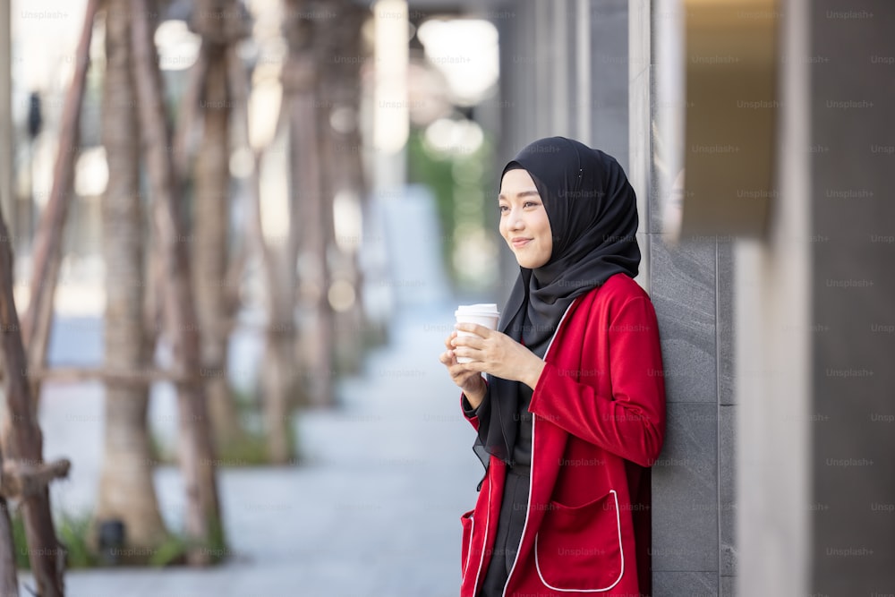 Donna musulmana moderna che attraversa la strada con un caffè da asporto