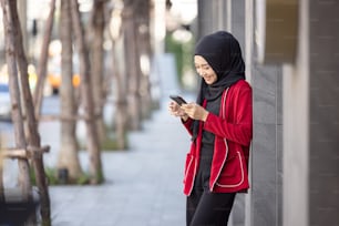 Jeune femme musulmane célébrant le succès en tenant un téléphone portable debout dans la rue