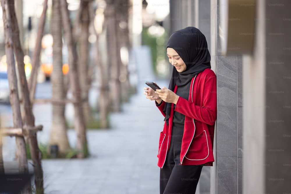 Jovem muçulmana que celebra o sucesso segurando o telefone celular em pé na rua