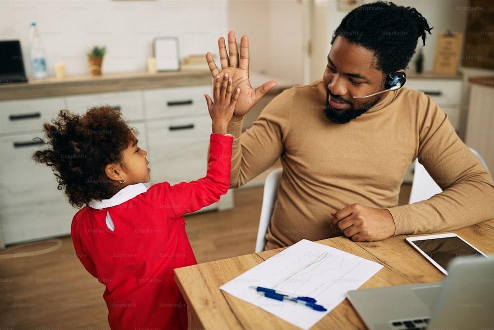 Felice padre single afroamericano che dà il cinque a sua figlia mentre lavora a casa.