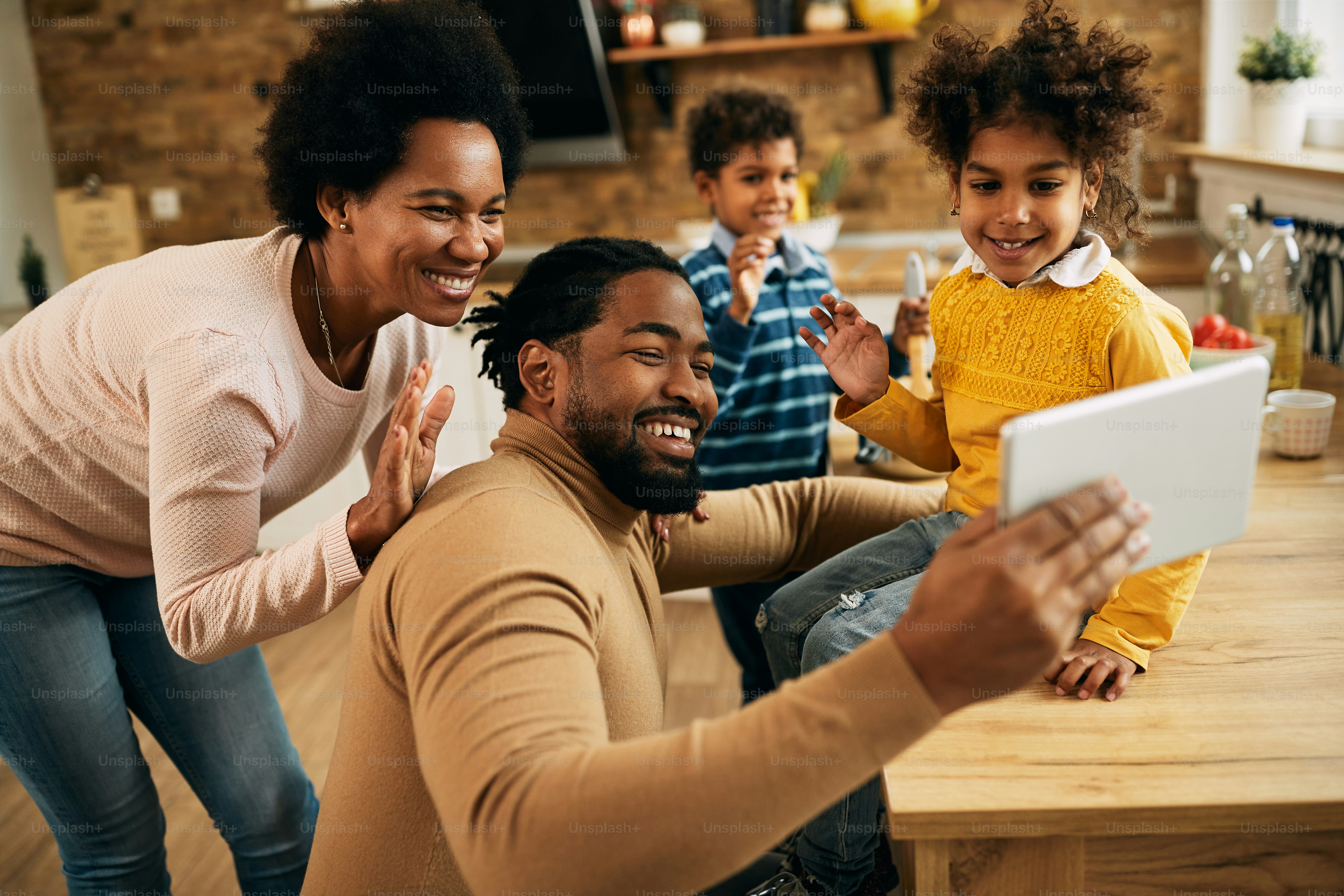 Happy African American family using touchpad and waving during video call.