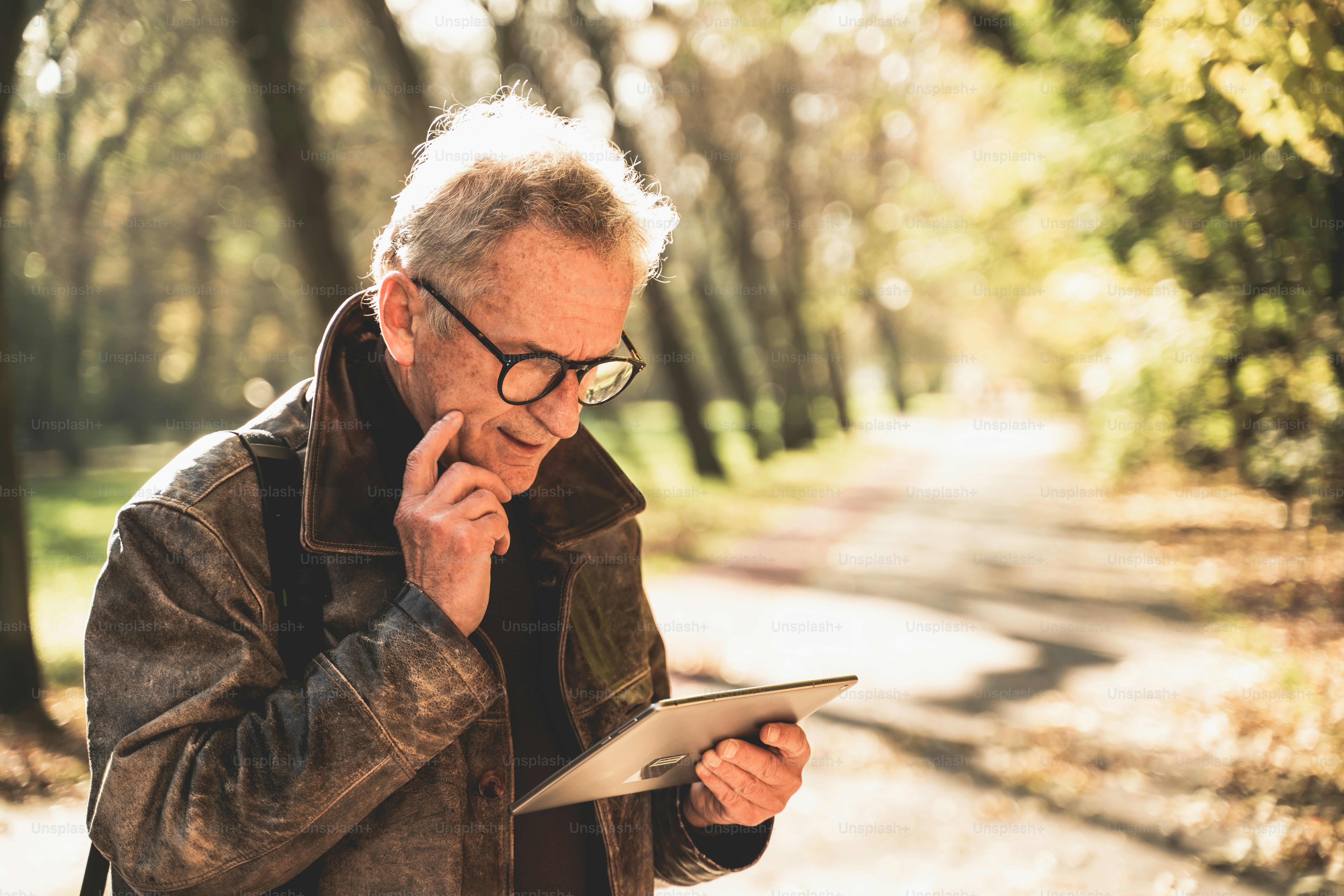 Handsome senior businessman working on tablet outdoor in park.