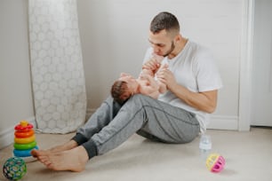 Fathers Day holiday. Caucasian father playing kissing  newborn baby. Parent holding rocking cute funny child daughter son. Authentic lifestyle candid tender moment. Single dad family life.