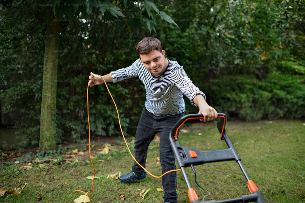 Portrait of down syndrome adult man mowing lawn outdoors in backyard, helping with housework concept.