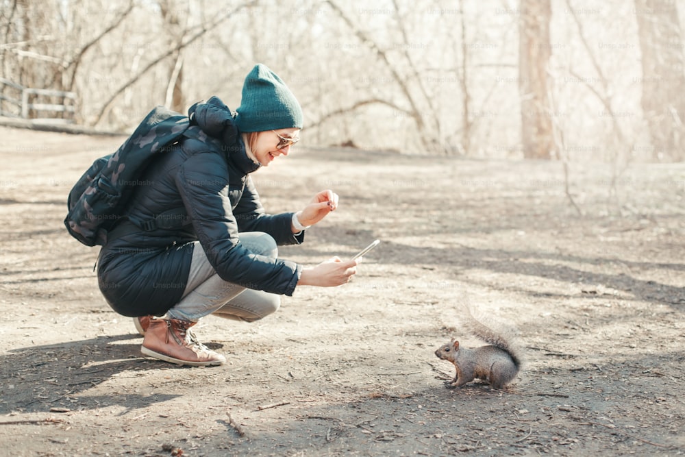 공원에서 다람쥐의 사진 사진을 찍는 백인 여성. 숲에서 야생 동물의 스마트폰 사진을 찍는 관광 여행자 소녀. 재미있는 야외 활동 및 온라인 블로깅 블로깅.