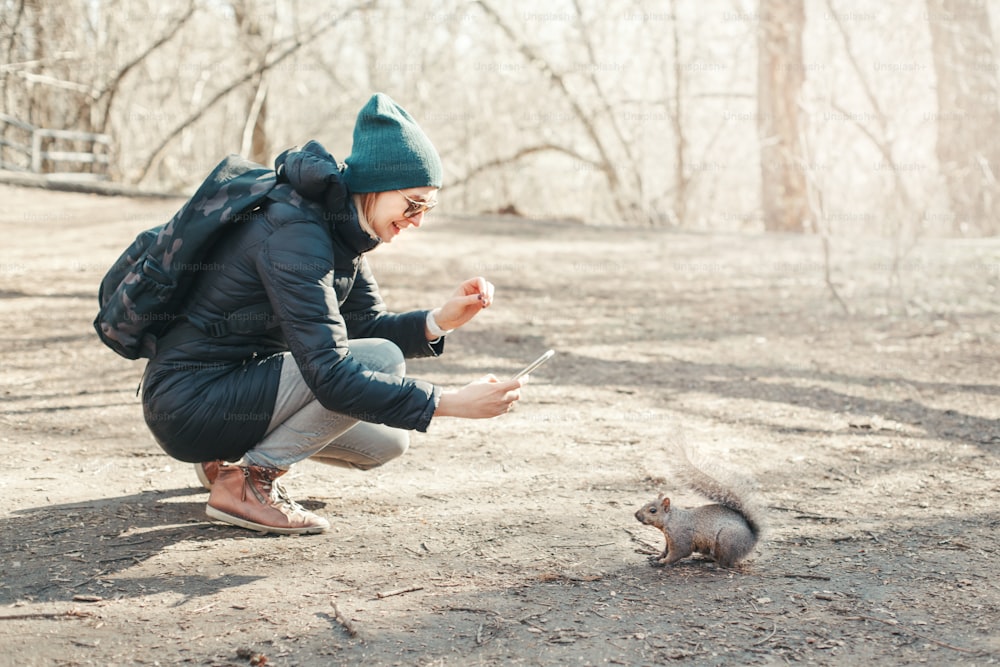 Caucasian woman taking picture photo of squirrel in park. Tourist traveler girl snapping smartphone photos of wild animal in forest. Fun outdoor activity and blogging vlogging online.