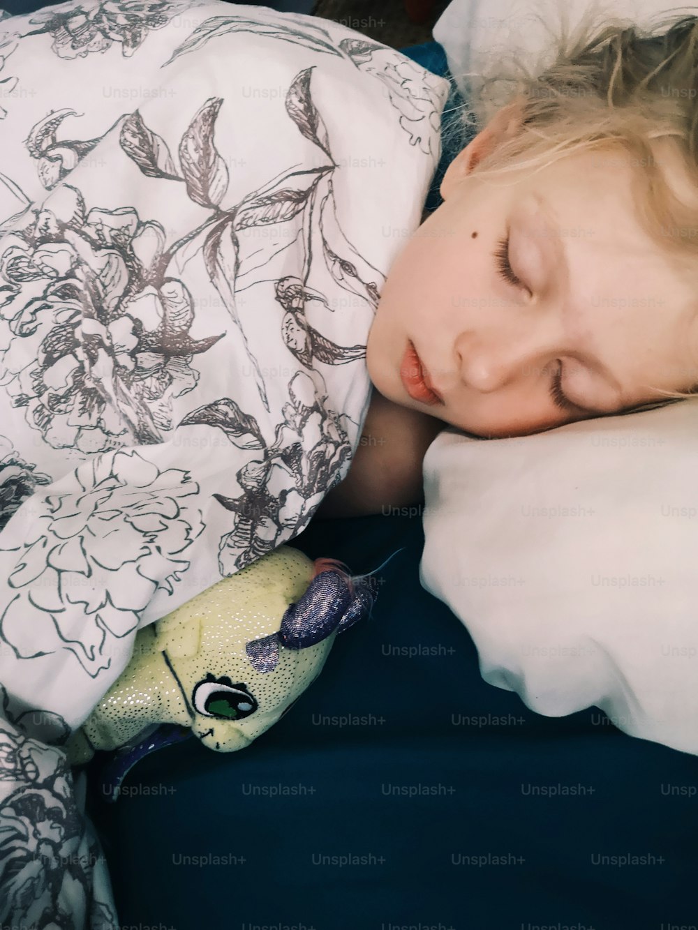 自宅のベッドでお気に入りのおもちゃと一緒に寝ているかわいい愛らしい小さな子供の女の子。睡眠補助玩具と一緒に夢を見ている子供。いい夢、見てね。